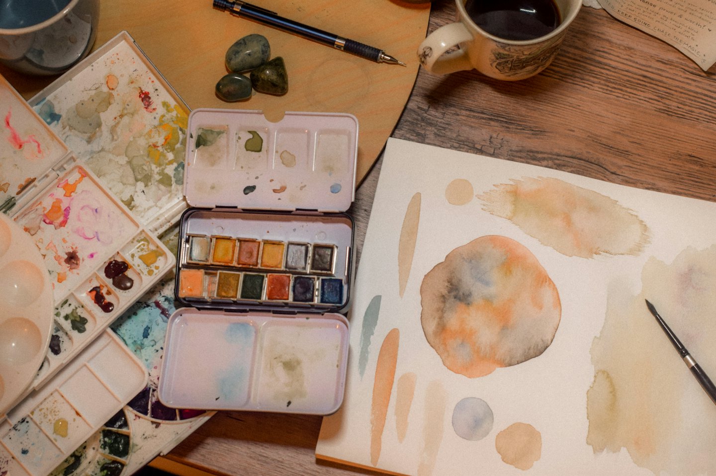 Artist's wooden desk with watercolor paints and coffee.