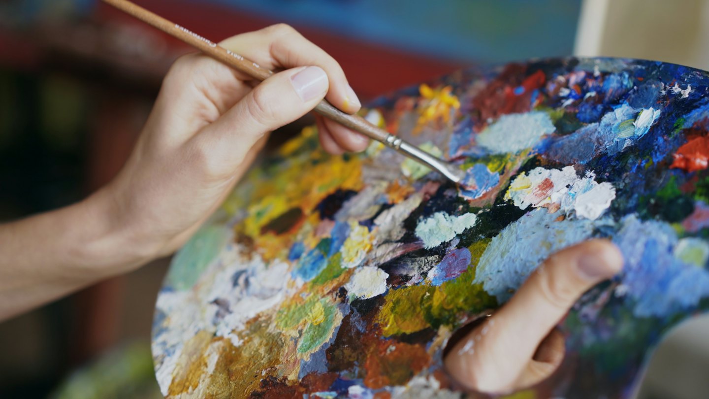 Artist holds a wooden palette with mixed oil paints.